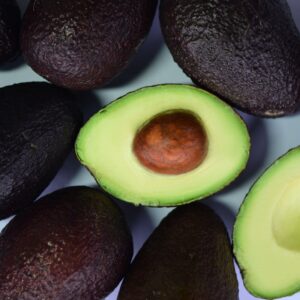 Top view of fresh avocados and cut halves on a white surface, showcasing their vibrant green color.